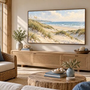 May include: A rectangular television mounted on a wall displaying a coastal landscape with sand dunes and ocean waves. Below the television is a long wooden media console with three woven cane cabinet doors and a light natural wood finish.
