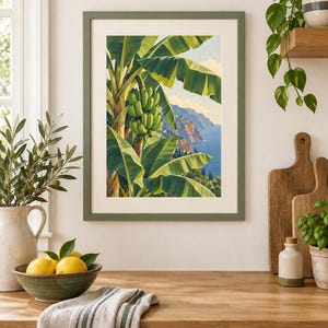 May include: A framed wall art print featuring a vibrant illustration of a banana tree with a large bunch of green bananas, set against a coastal landscape with blue water, distant cliffs, and a clear sky, enclosed in a matte olive green frame.