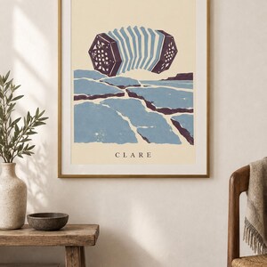 May include: A framed wall art print featuring a stylized illustration of a concertina musical instrument floating above a blue and dark purple landscape. The word CLARE is printed in black capital letters at the bottom of the cream-colored background.