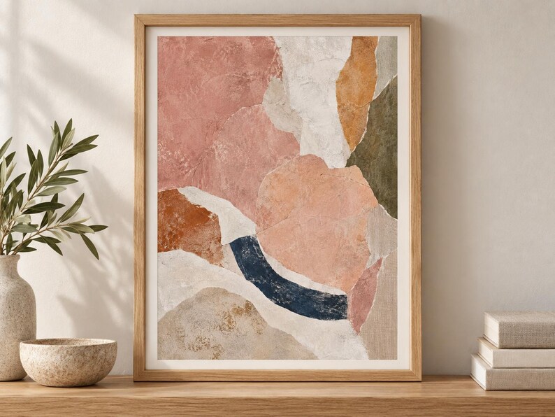 May include: A framed abstract wall art print featuring a collage of organic shapes in muted tones of dusty pink, terracotta, cream, olive green, and a dark navy blue curved accent, all set within a light-toned wooden frame with a white mat border.