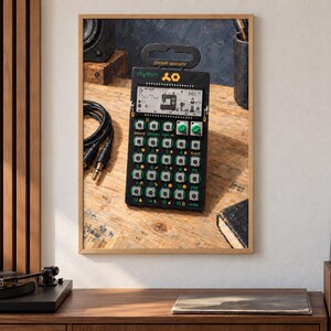 May include: A black pocket operator rhythm drum machine featuring a digital LCD screen, a grid of small silver buttons, two green rotary knobs, and yellow text labels. The device has a top handle and displays the text rhythm and pocket operator.