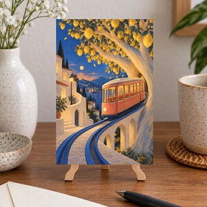 K&ouml;nnte beinhalten: Ein rechteckiger Kunstdruck auf einer Holzstaffelei zeigt eine korallenfarbene Stra&szlig;enbahn, die in der D&auml;mmerung auf blauen Schienen durch eine K&uuml;stenstadt f&auml;hrt. Ein gro&szlig;er Zitronenbaum mit gelben Fr&uuml;chten w&ouml;lbt sich &uuml;ber die Bahn, im Hintergrund wei&szlig;e Geb&auml;ude.