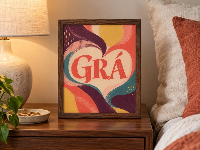 May include: A rectangular framed print featuring the word GR&Aacute; in large red letters centred within a cream-coloured heart shape. The background consists of abstract, flowing shapes in shades of yellow, red, teal, and deep purple with small yellow dashes.