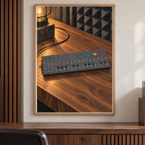 Op de afbeelding: Een rechthoekige donkergrijze elektronische synthesizer met een raster van ronde knoppen en vier opvallende gekleurde draaiknoppen in groen, blauw, geel en rood. Het apparaat wordt weergegeven in een houten lijst en toont de interface.
