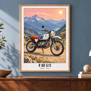 Pu&ograve; includere: Una stampa d'arte incorniciata raffigurante una moto BMW R 80 G/S bianca con sella rossa e dettagli blu su un sentiero sterrato. Lo sfondo mostra una catena montuosa sotto un cielo al tramonto. Il testo in basso riporta R 80 G/S BMW 1980.