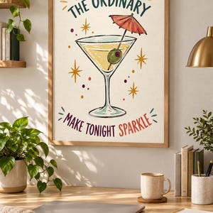 May include: A framed wall art print featuring a martini glass with an olive and a red cocktail umbrella. The text reads SHAKE UP THE ORDINARY and MAKE TONIGHT SPARKLE in red and dark green. The illustration includes yellow starbursts and dots.