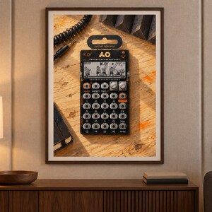 Op de afbeelding: Een zwarte Teenage Engineering PO-33 K.O. pocket operator sampler en sequencer met een monochroom LCD-scherm dat de tekst K.O. weergeeft, een raster van zestien ronde knoppen, twee zilveren draaiknoppen en oranje accenten, ingelijst als wandkunst.