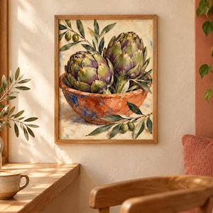 May include: A framed wall art print featuring a painting of two green and purple artichokes resting in a rustic, textured orange bowl. The composition includes sprigs of green olive leaves and small olives, set against a light, neutral background.