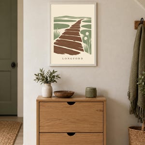Puede incluir: Una l&aacute;mina de arte mural enmarcada que presenta una ilustraci&oacute;n estilizada de un camino de madera que serpentea a trav&eacute;s de un paisaje verde con el texto LONGFORD impreso en la parte inferior. La obra utiliza una paleta de colores marr&oacute;n, verde salvia y crema.