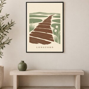 Puede incluir: Una l&aacute;mina de arte mural enmarcada que presenta una ilustraci&oacute;n de paisaje estilizada de un camino de madera marr&oacute;n que conduce a una zona pantanosa verde con hierbas altas, sobre un fondo crema con el texto LONGFORD impreso en la parte inferior.