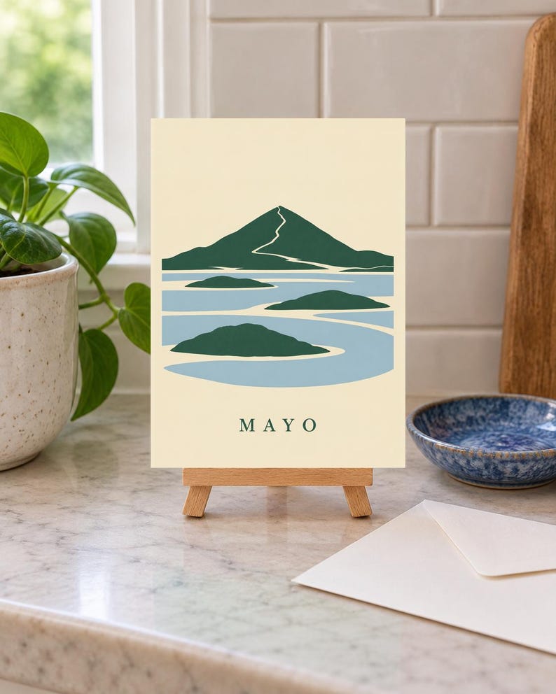 Pu&ograve; includere: Una stampa artistica rettangolare su un piccolo cavalletto in legno con un'illustrazione stilizzata di una montagna e isole in verde scuro e azzurro su sfondo crema. La parola MAYO &egrave; stampata in lettere maiuscole verde scuro in basso.