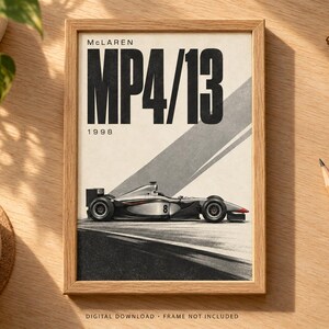 May include: A framed poster featuring a side profile of a silver and black McLaren MP4/13 Formula 1 race car with the number 8 on the side. The text reads McLaren MP4/13 and 1998. The design includes a diagonal gray stripe on a cream background.