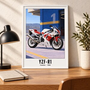 May include: A framed wall art print featuring a white and red Yamaha YZF-R1 motorcycle from 1998. The motorcycle is parked in front of a blue wall with a yellow stripe and the number one. The text YZF-R1 Yamaha 1998 is printed at the bottom.