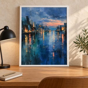May include: A framed wall art print featuring an impressionistic cityscape at twilight. The painting displays dark blue and teal water reflecting golden city lights and a sunset sky with orange and pink hues above a silhouetted urban skyline.