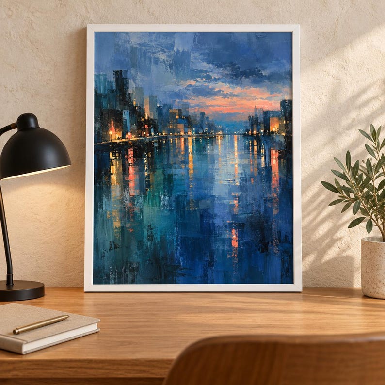 May include: A framed wall art print featuring an impressionistic cityscape at twilight. The painting displays dark blue and teal water reflecting golden city lights and a sunset sky with orange and pink hues above a silhouetted urban skyline.