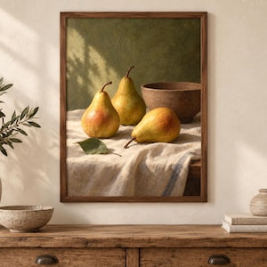 May include: A framed wall art print featuring a still life composition of three yellow and red pears resting on a textured white linen cloth next to a brown wooden bowl. The background is a muted olive green with soft shadows cast across the scene.