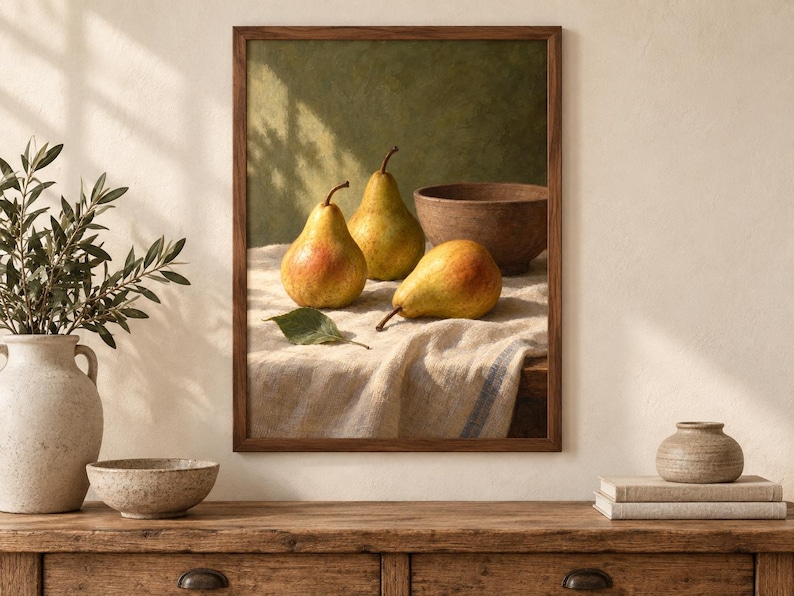 May include: A framed wall art print featuring a still life composition of three yellow and red pears resting on a textured white linen cloth next to a brown wooden bowl. The background is a muted olive green with soft shadows cast across the scene.