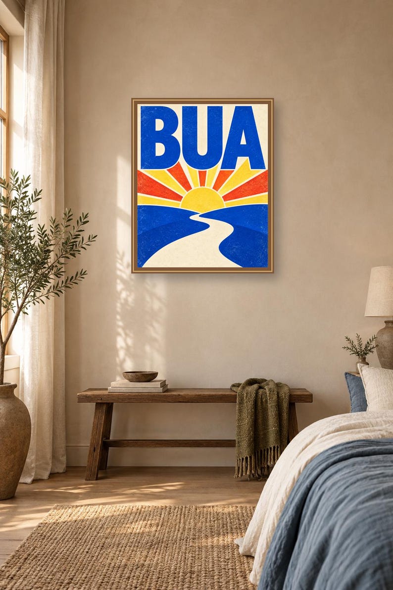 May include: A rectangular wall art print in a thin brown frame featuring the text BUA in large blue letters above a stylized yellow sun rising over a winding white path that cuts through blue hills with red and yellow sunburst rays.