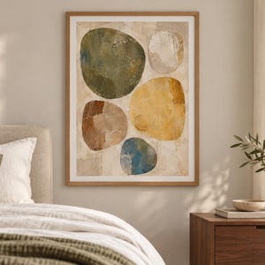 May include: A framed wall art print featuring an abstract composition of five large, rounded organic shapes in shades of olive green, mustard yellow, terracotta brown, muted blue, and off-white, set against a textured, neutral-toned background.