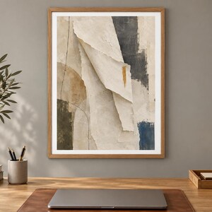 May include: A framed abstract wall art print featuring layered paper-like textures in shades of cream, beige, and charcoal gray. The composition includes a prominent vertical fold, a thin black line, and a small gold brushstroke accent.