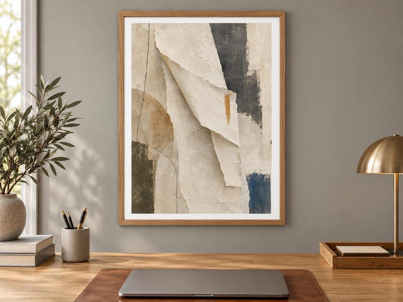 May include: A framed abstract wall art print featuring layered paper-like textures in shades of cream, beige, and charcoal gray. The composition includes a prominent vertical fold, a thin black line, and a small gold brushstroke accent.