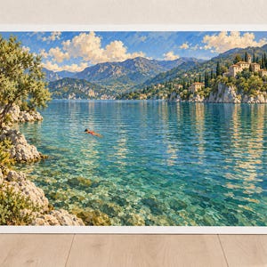 May include: A framed landscape painting depicting a clear blue lake surrounded by rocky cliffs and lush green trees. A small figure swims in the center of the water. In the distance, stone buildings sit atop a cliff under a bright blue sky with clouds.
