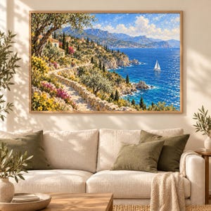 May include: A rectangular landscape painting in a wooden frame depicting a coastal scene with a stone path winding along a cliffside, vibrant yellow and pink flowers, olive trees, a blue sea, distant mountains, and a single white sailboat.