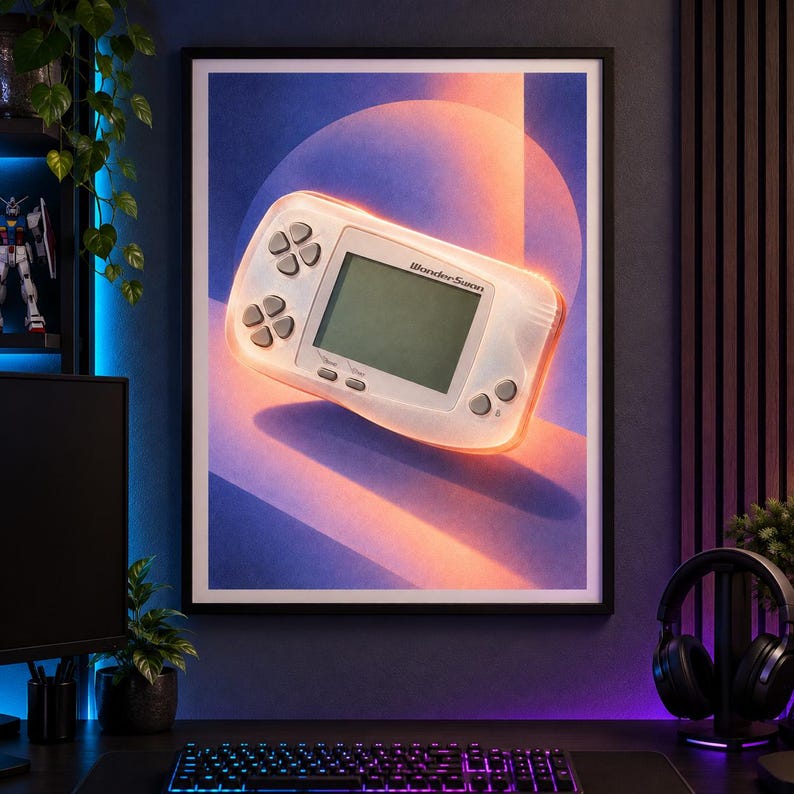 Pu&ograve; includere: Una stampa artistica da parete incorniciata raffigurante una console di gioco portatile WonderSwan bianca centrata su uno sfondo di forme geometriche blu e arancioni con un effetto luminoso circolare. La console ha uno schermo e pulsanti grigi.