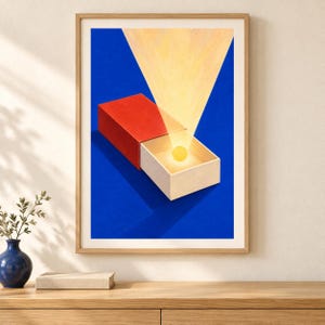 May include: A framed art print featuring a red matchbox against a deep blue background. The drawer of the matchbox is partially open, revealing a glowing yellow sphere inside, with a bright yellow light beam projecting upward from the centre.
