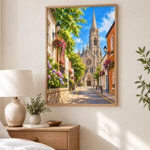 Pu&ograve; includere: Una stampa d'arte da parete incorniciata che raffigura una stretta strada europea con un'alta chiesa in pietra dotata di rosone e guglia. La strada &egrave; fiancheggiata da edifici in mattoni, cesti di fiori appesi, alberi verdi e lampioni in ferro.