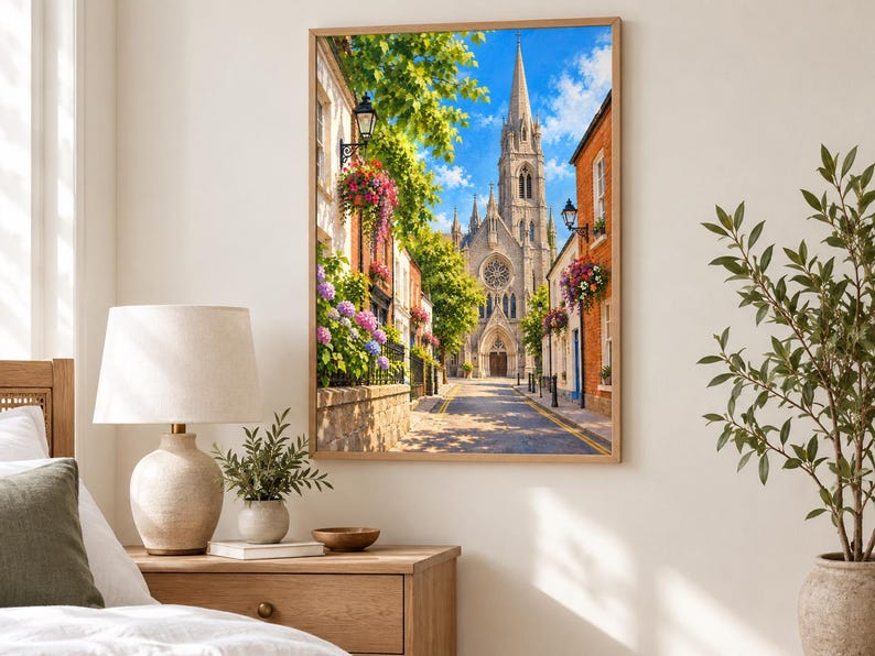 Pu&ograve; includere: Una stampa d'arte da parete incorniciata che raffigura una stretta strada europea con un'alta chiesa in pietra dotata di rosone e guglia. La strada &egrave; fiancheggiata da edifici in mattoni, cesti di fiori appesi, alberi verdi e lampioni in ferro.
