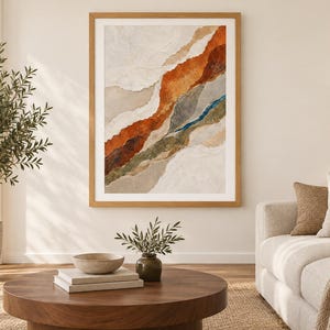 May include: A framed abstract wall art piece featuring layered, torn-paper style textures in shades of burnt orange, deep brown, muted green, and cream. The composition displays diagonal, organic bands of color with a thin, vibrant blue accent line.
