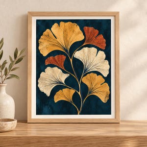May include: A framed wall art print featuring a botanical illustration of ginkgo leaves in shades of gold, rust orange, and cream against a dark navy blue textured background. The artwork is enclosed in a light-toned wooden frame with a clean border.