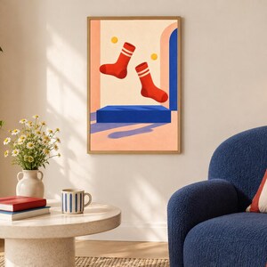 May include: A framed wall art print featuring a graphic illustration of two red socks with white stripes floating above a solid blue rectangular platform. The background consists of a light peach wall with a blue archway and two small yellow circles.