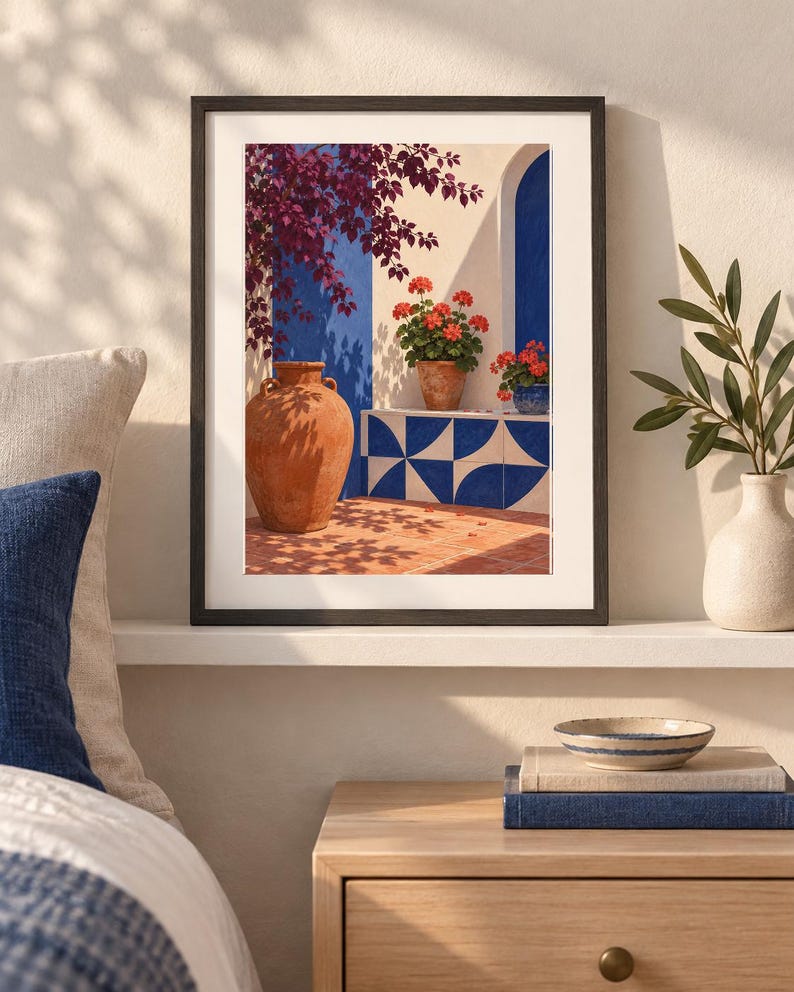 Pu&ograve; includere: Una stampa d'arte incorniciata che raffigura una scena mediterranea con una grande anfora in terracotta, gerani rossi in vaso e piastrelle geometriche blu e bianche. L'opera mostra un cortile soleggiato con accenti blu sulle pareti.
