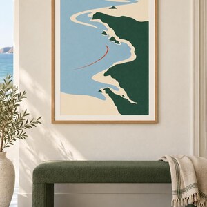 May include: A framed wall art print featuring a stylized coastal landscape with a light blue ocean, beige sandy shoreline, and dark green landmasses. A thin, curved red line is positioned in the water. The print is encased in a light wood frame.