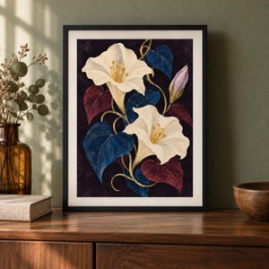 Puede incluir: Una l&aacute;mina de arte enmarcada que muestra dos grandes flores en forma de trompeta de color crema con centros amarillos. La ilustraci&oacute;n floral incluye hojas en forma de coraz&oacute;n de color azul profundo y granate oscuro sobre un fondo morado oscuro, todo en un marco negro.