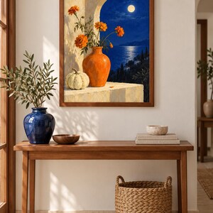 Puede incluir: Una impresi&oacute;n de arte mural enmarcada que representa una escena nocturna con luna llena sobre un mar azul oscuro. Un jarr&oacute;n naranja lleno de flores de cempas&uacute;chil naranjas y una calabaza blanca sobre una repisa de piedra bajo un arco.