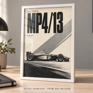 May include: A framed poster featuring a side profile of a silver and black McLaren MP4/13 Formula One race car with the number 8 on the side. The text reads McLaren MP4/13 1998 in bold black lettering against a cream background with diagonal gray lines.