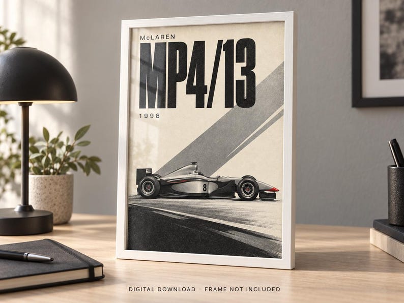 May include: A framed poster featuring a side profile of a silver and black McLaren MP4/13 Formula One race car with the number 8 on the side. The text reads McLaren MP4/13 1998 in bold black lettering against a cream background with diagonal gray lines.