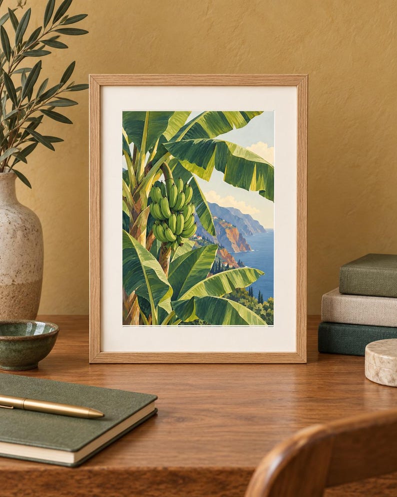 May include: A framed art print featuring a vibrant illustration of a banana tree with a cluster of green bananas, set against a backdrop of a coastal landscape with blue ocean waters, rocky cliffs, and a clear sky with soft white clouds.