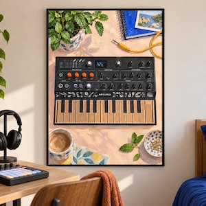 May include: A framed wall art print featuring a digital illustration of a black Arturia synthesizer with orange knobs and a cork-textured keyboard. The scene includes a potted plant, a blue notebook, a yellow cable, a coffee mug, and paper clips.