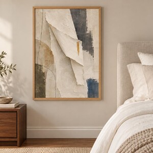 May include: A rectangular wall art piece in a light wood frame featuring an abstract composition of layered, torn-paper textures in shades of cream, beige, charcoal gray, and deep blue, accented by a single vertical gold brushstroke mark.