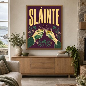 Pu&ograve; includere: Una stampa artistica da parete rettangolare con sfondo viola scuro e la parola SL&Aacute;INTE in grandi lettere gialle. L'illustrazione raffigura due mani che tengono dei bicchieri in un brindisi, circondate da trifogli verdi e piccoli fiori bianchi.