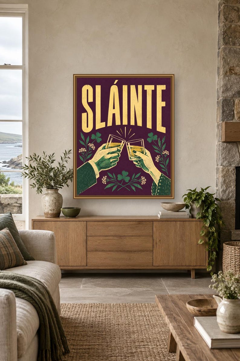 Pu&ograve; includere: Una stampa artistica da parete rettangolare con sfondo viola scuro e la parola SL&Aacute;INTE in grandi lettere gialle. L'illustrazione raffigura due mani che tengono dei bicchieri in un brindisi, circondate da trifogli verdi e piccoli fiori bianchi.