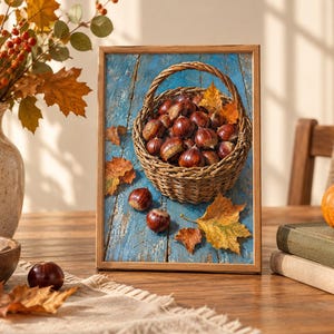 May include: A rectangular framed print featuring a woven wicker basket filled with brown chestnuts resting on a weathered blue wooden surface. Several loose chestnuts and fallen autumn leaves in shades of yellow and orange are scattered around the basket.
