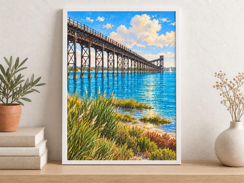 Peut inclure: Une impression d'art encadr&eacute;e repr&eacute;sentant un long pont &agrave; chevalets en bois s'&eacute;tendant au-dessus d'une eau bleu vif. Le premier plan pr&eacute;sente des herbes c&ocirc;ti&egrave;res vertes et des arbustes bas sous un ciel bleu vif avec des nuages blancs.