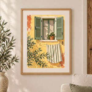 May include: A framed wall art print depicting a yellow stucco wall with an open window featuring green shutters and a potted plant. A white and green striped towel hangs on a clothesline below the window, with olive tree branches in the foreground.