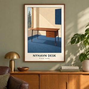 May include: A framed art print featuring a wooden desk with black legs and a three-drawer unit on a blue floor. The scene includes a window view of trees and a blue wall panel. The text reads NYHAVN DESK and Finn Juhl in black lettering.