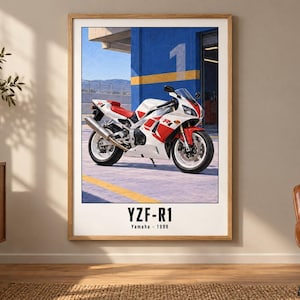 May include: A framed wall art print featuring a white and red Yamaha YZF-R1 motorcycle parked in front of a blue building with a yellow stripe and the number one. The text YZF-R1 and Yamaha 1998 is printed in black at the bottom of the white poster.
